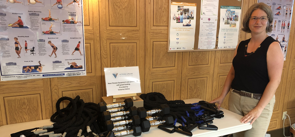 Lifeline staff member stands next to a table full of exercise equipment funded by the Health Promotion Grant.