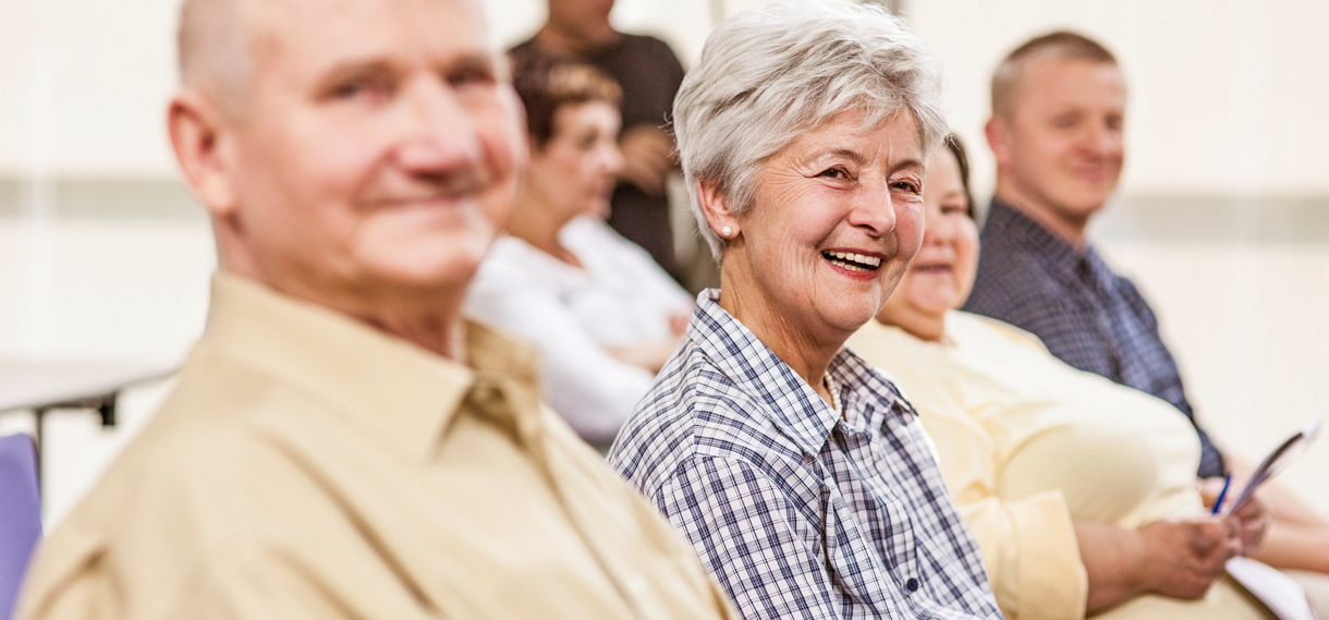 Group of smiling older adults sitting on a row of chairs.