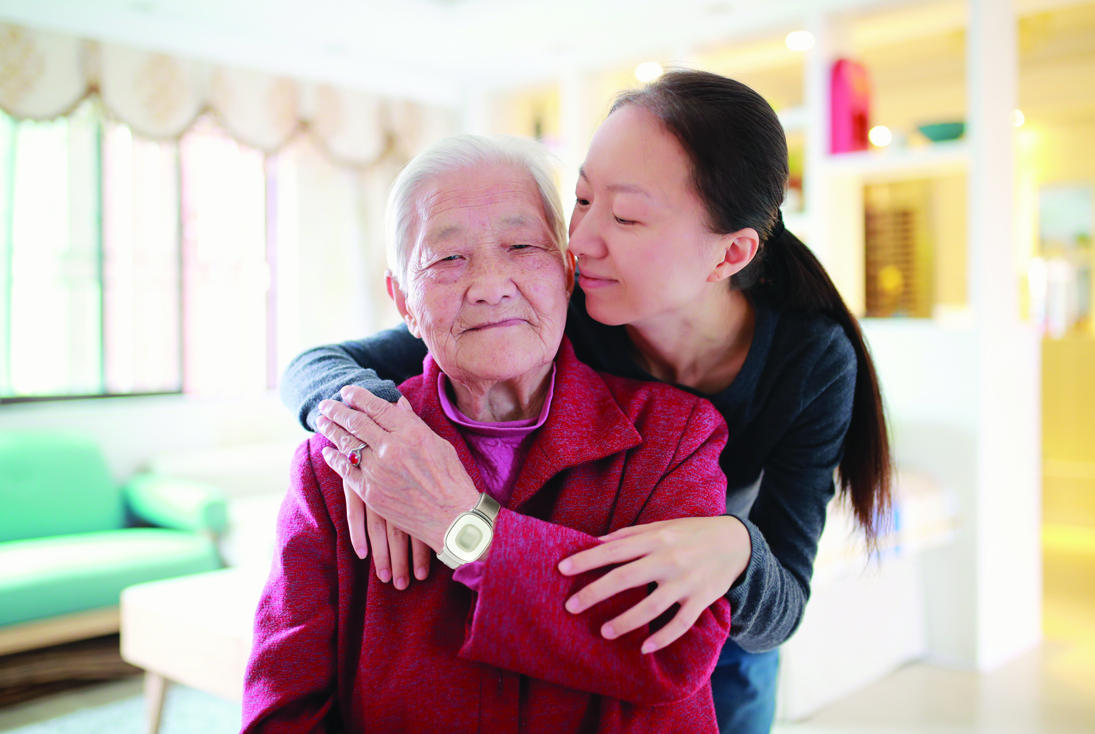 Asian grandaughter embracing her grandmother, who is wearing the Home Safe wrist bracelet.