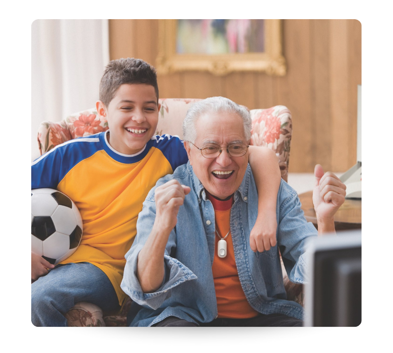 Older Man with grandchild watching soccer together cheering. While wearing a Lifeline Button.